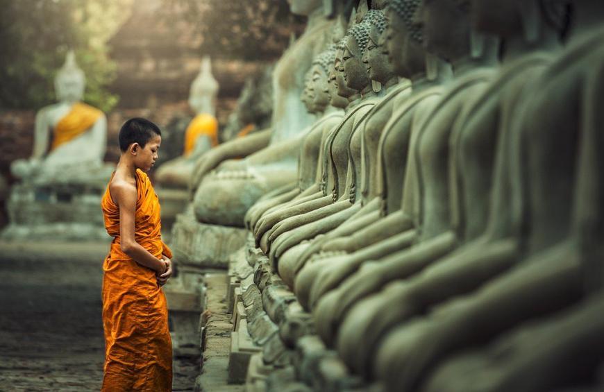Buddhister förespråkar fasta och avhållsamhet. Statyer. Ung pojke ber eller mediterar.