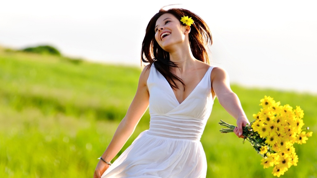 Snygg tjej i vit klänning skrattar i sommaren med blommor i handen.